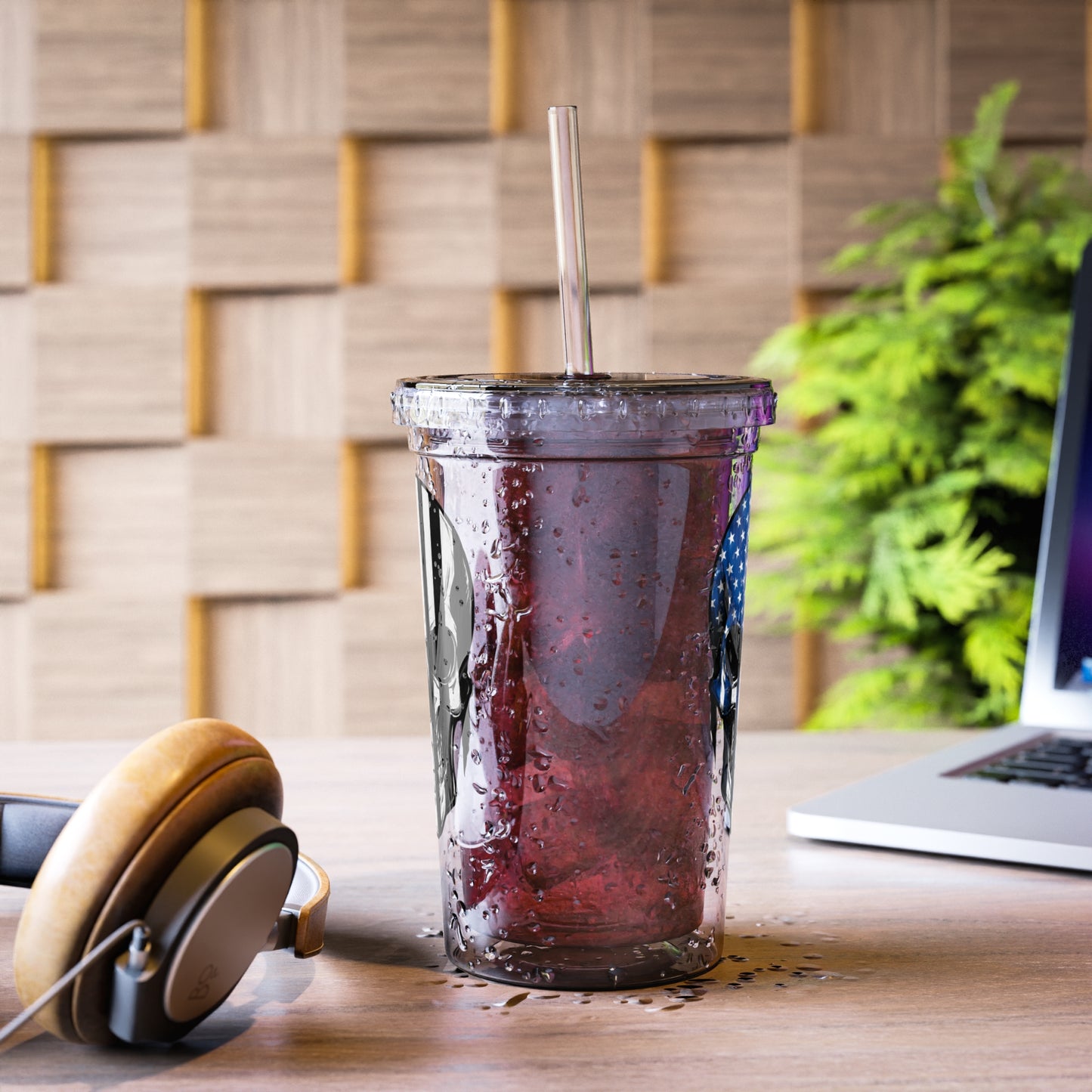 Energy drink in a clear cup with a straw on a desk with headphones and a laptop.