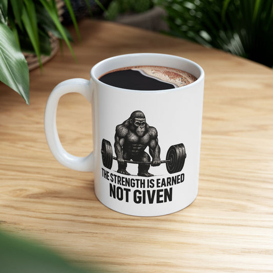 Person holding a mug with Strength Is Earned gorilla gym graphic.