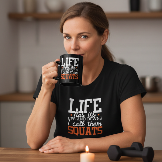 Woman wearing a black t-shirt with humorous text, holding a mug in a kitchen setting.