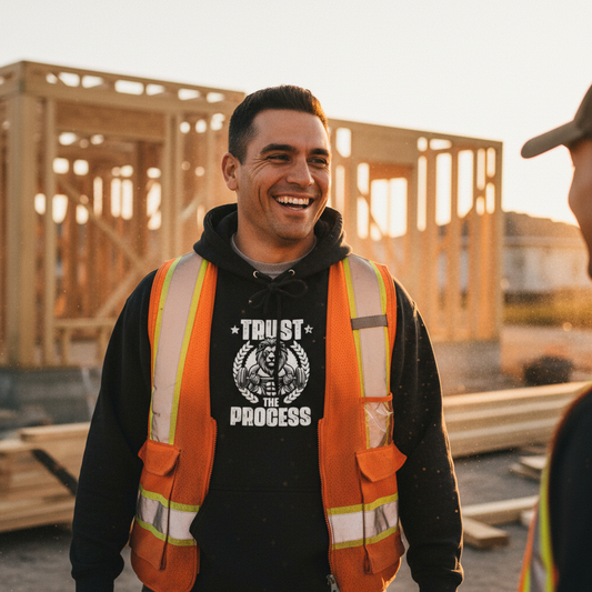 Man in safety vest and hoodie with 'Trust the Process' shirt at a construction site