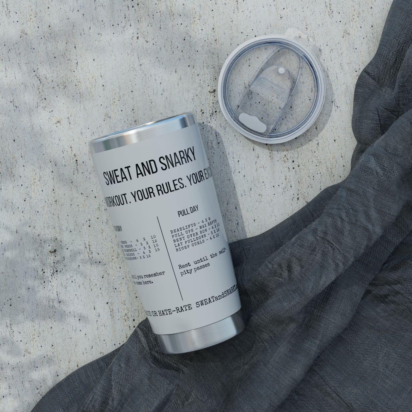 Silver tumbler with text on a concrete surface with a gray sweatshirt.