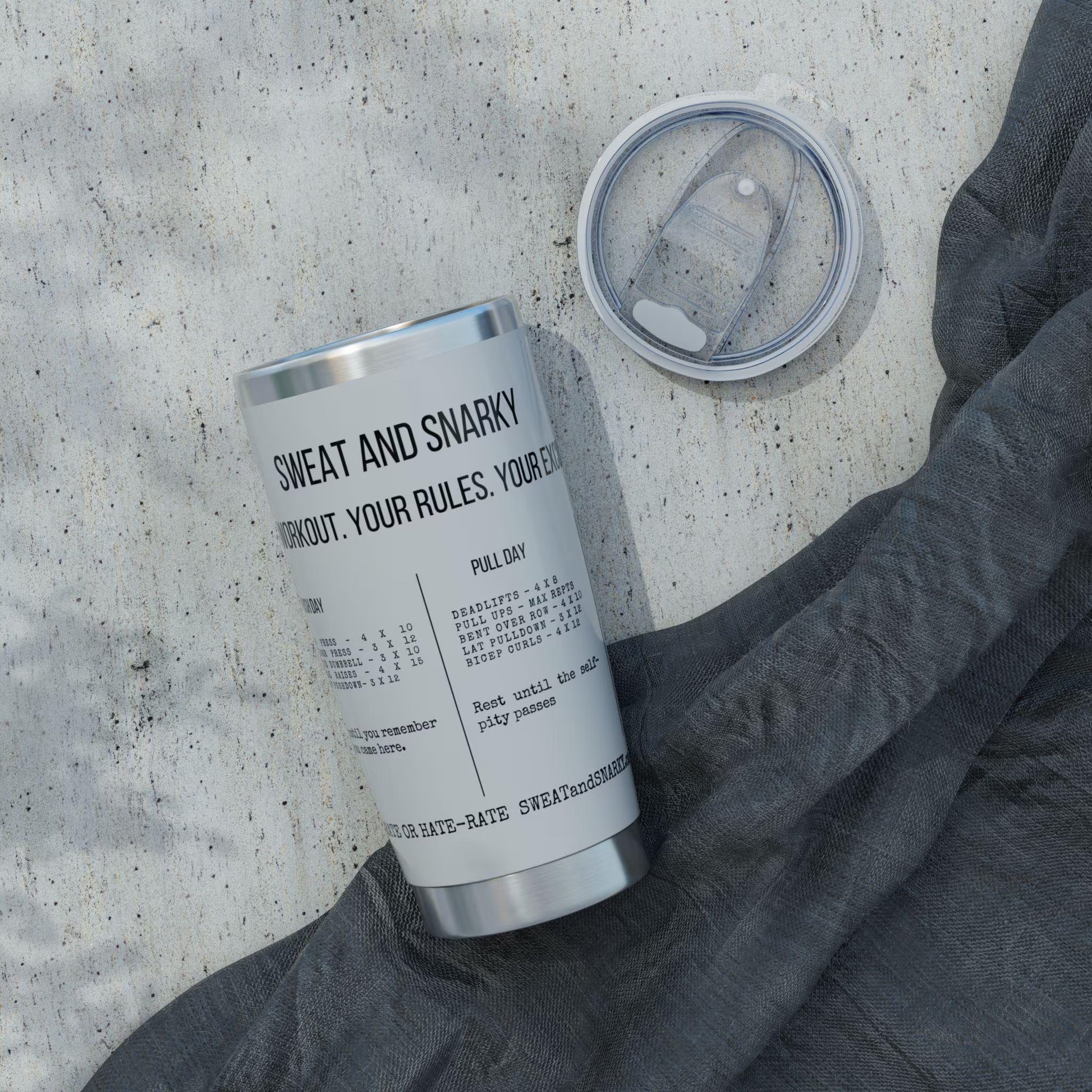 Silver tumbler with text on a concrete surface with a gray sweatshirt.